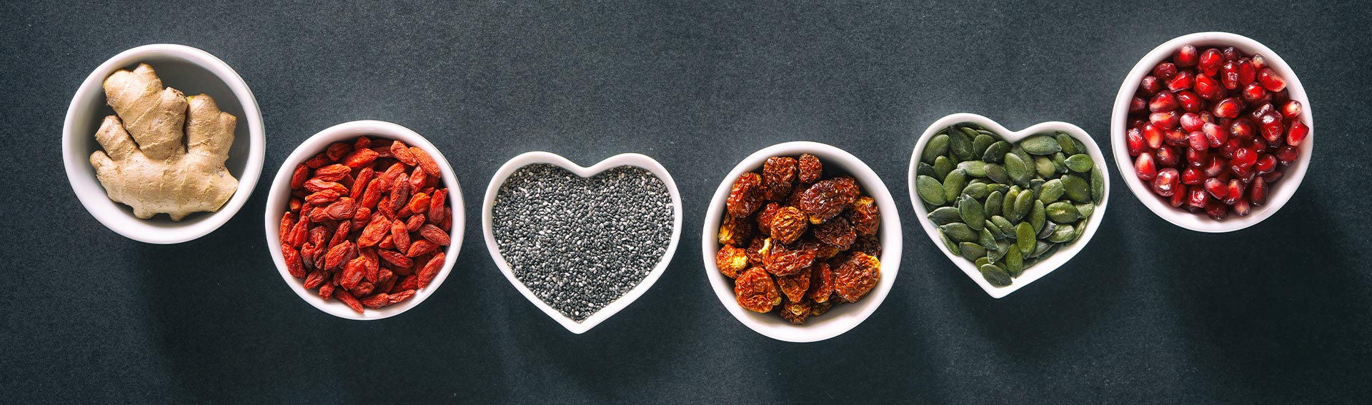 Cups of healthy foods on top of a dark grey table, with two cups shaped like hearts.
